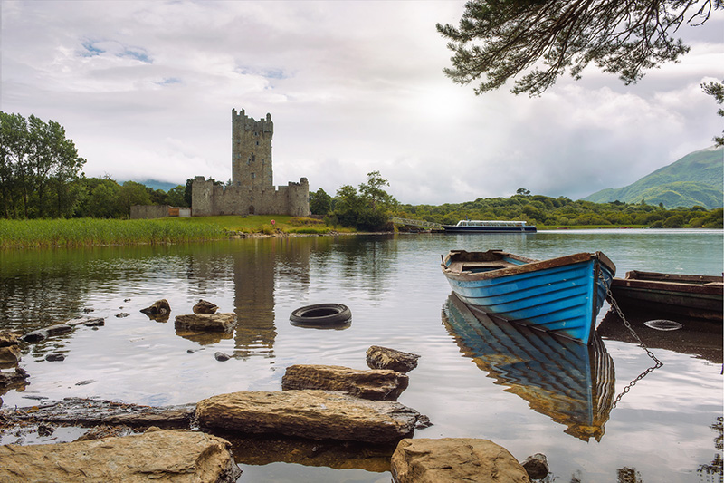 Ross Castle ruins and the Lough Leane lake with a blue boat in the foreground in the Killarney National Park, Ireland